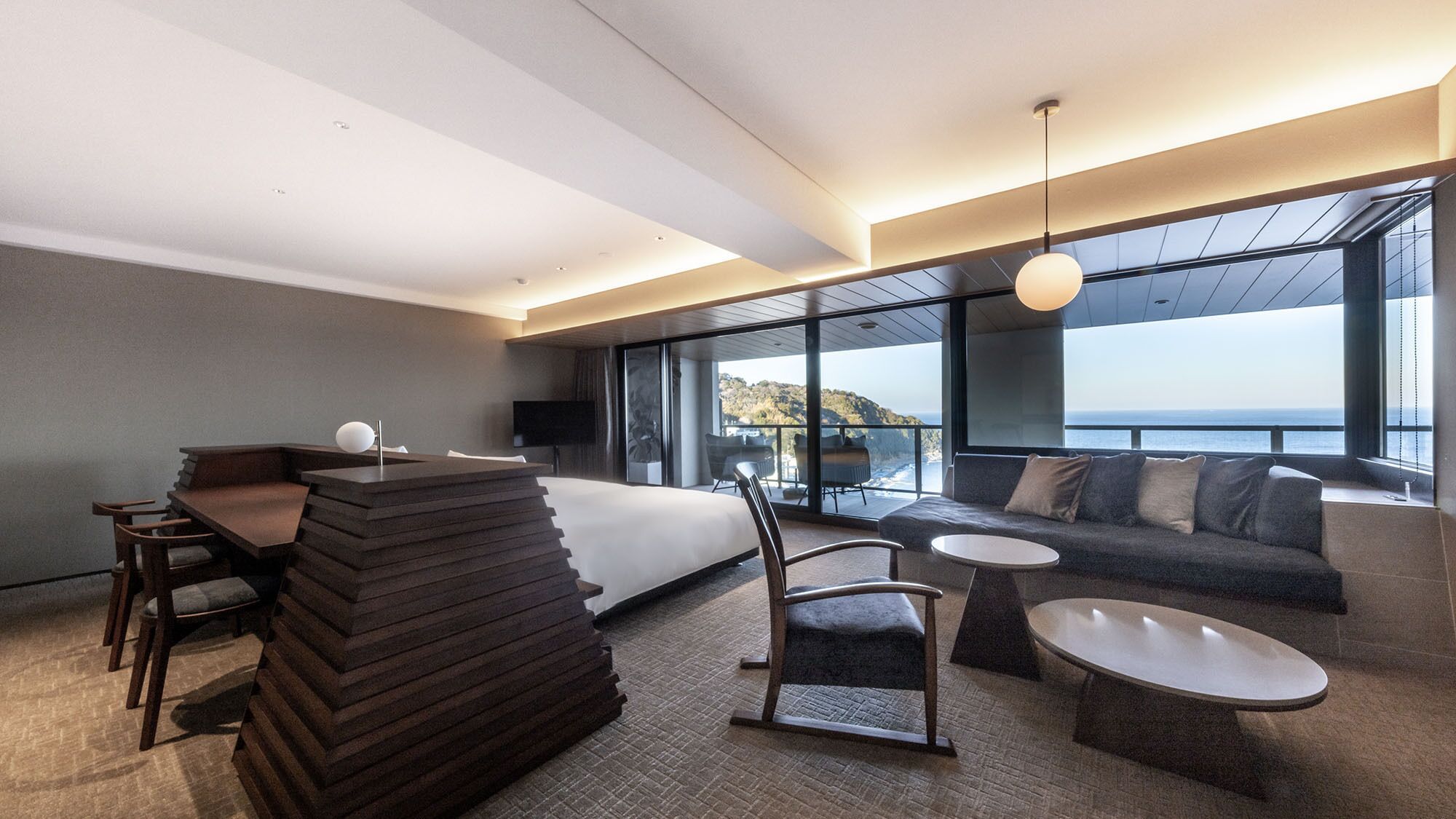 Habitación de hotel moderna con cama, zona de estar y un amplio ventanal con vista al mar.