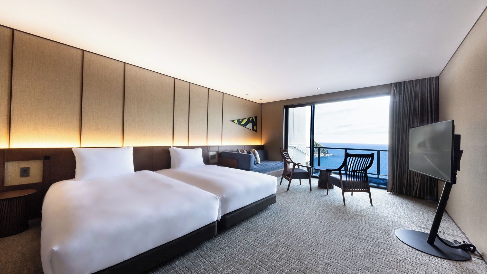 Une chambre d’hôtel avec deux lits, une télévision, un coin salon avec vue sur la mer et un balcon.