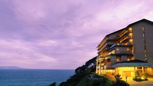 A multi-story hotel with balconies, a view of the sea, and a landscaped garden area. - Atagawa Onsen Suiko (Higashiizu)