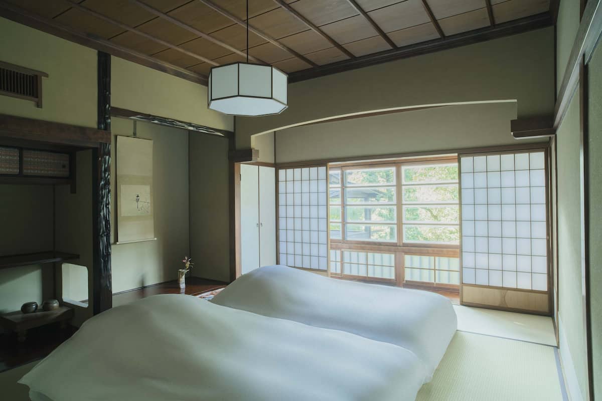A traditional Japanese room with tatami flooring, a low wooden bed, a shoji screen door, and a hanging lantern.