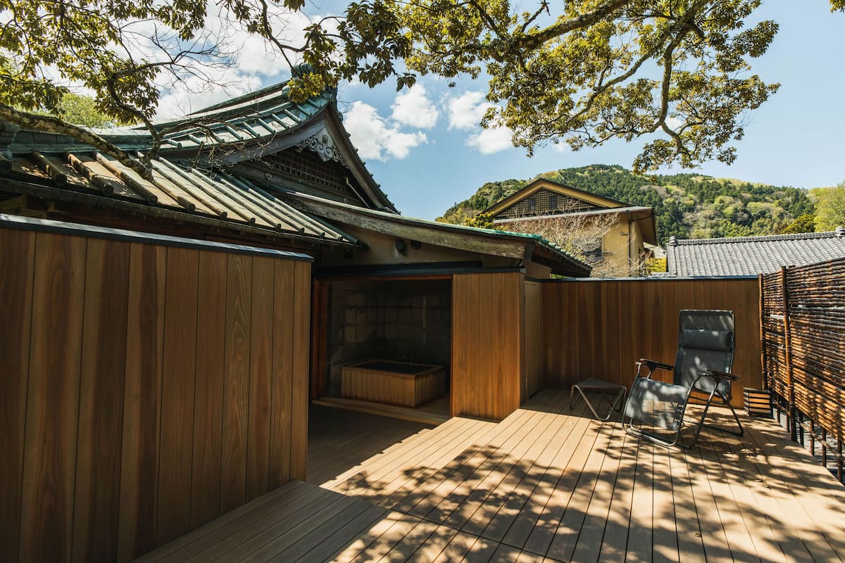 A traditional Japanese building with a wooden deck, a hot tub, and a view of a hillside.