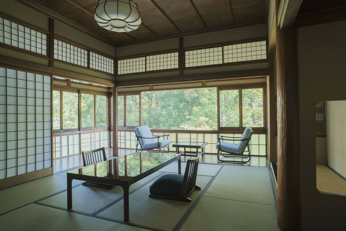 A traditional Japanese room with tatami flooring, a low table, and two chairs.