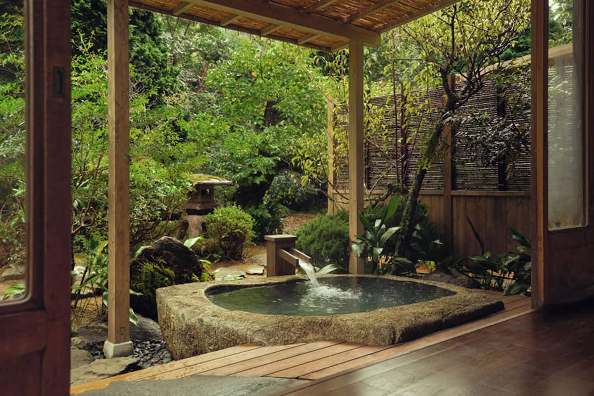 A traditional Japanese garden with a stone hot spring, wooden deck, and lush greenery.