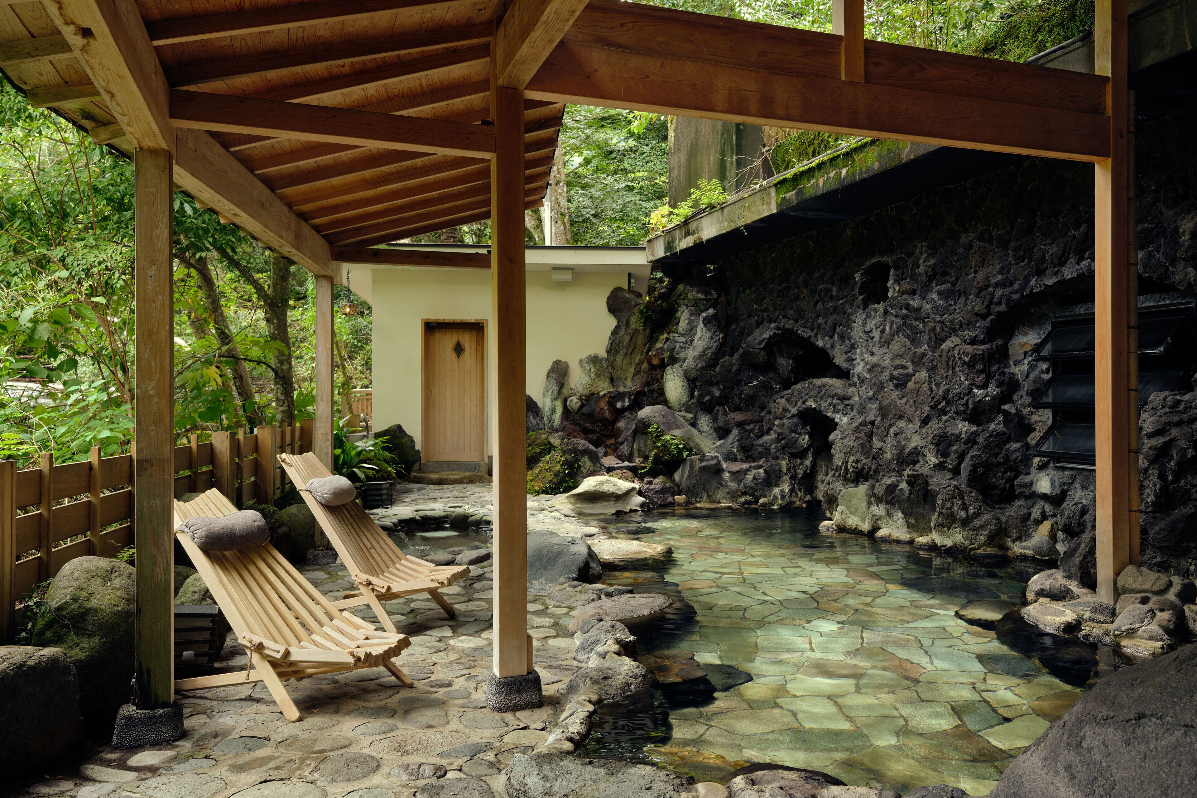 A stone-tiled outdoor spa area with wooden loungers and a wooden pergola.