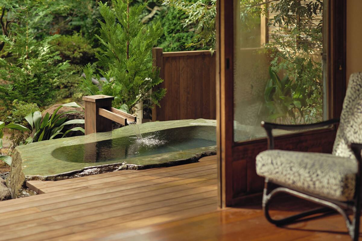 A wooden deck with a small pond, surrounded by lush greenery and a wooden fence.