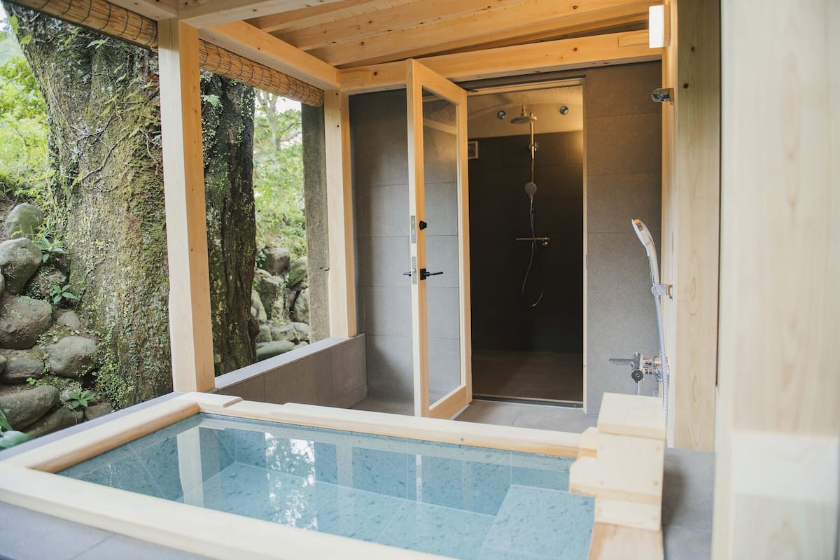 A spa area with a hot tub, a walk-in shower, and a view of a natural stone wall.