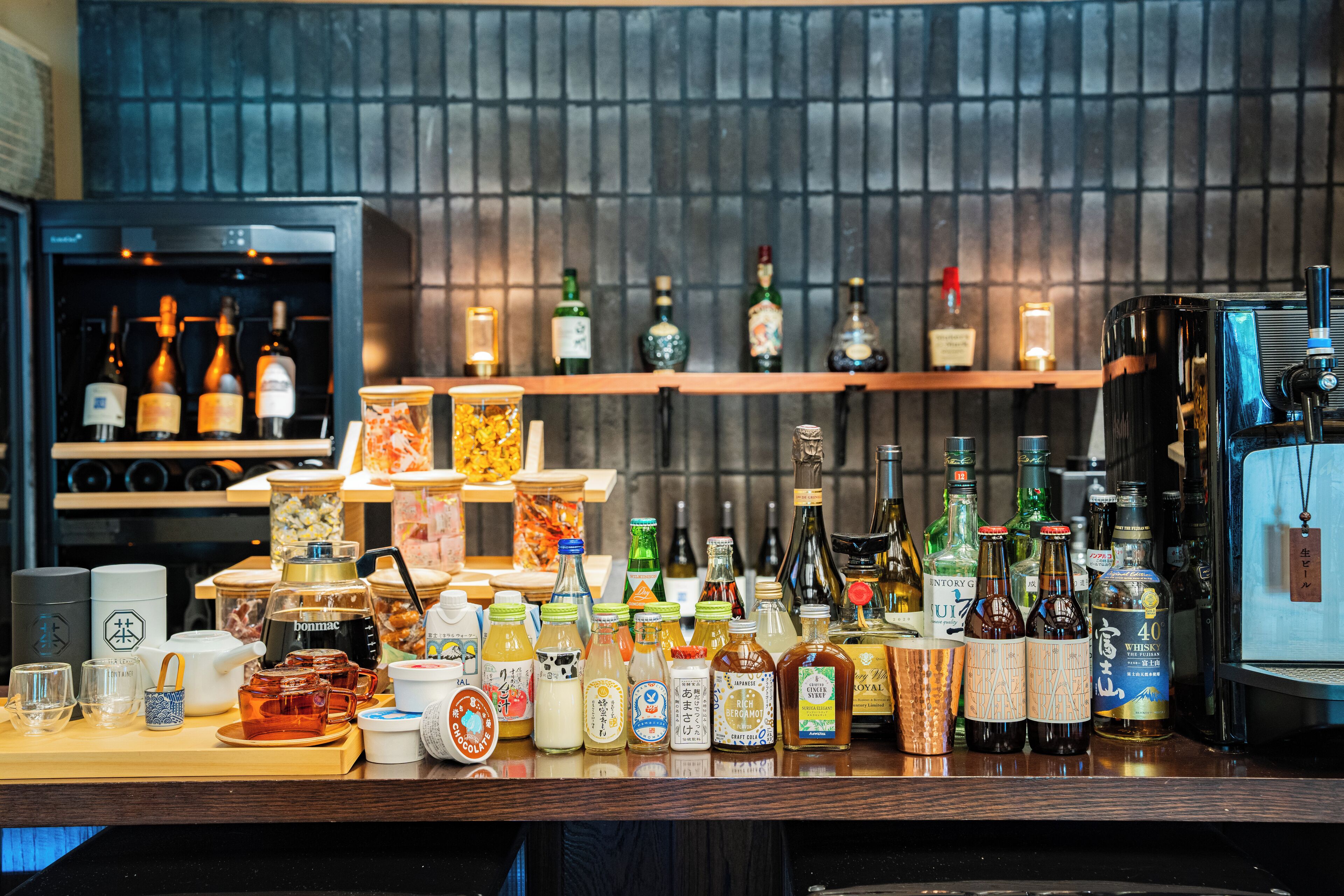 A bar area with various bottles and glasses, a coffee machine, and shelves with bottles in the background.