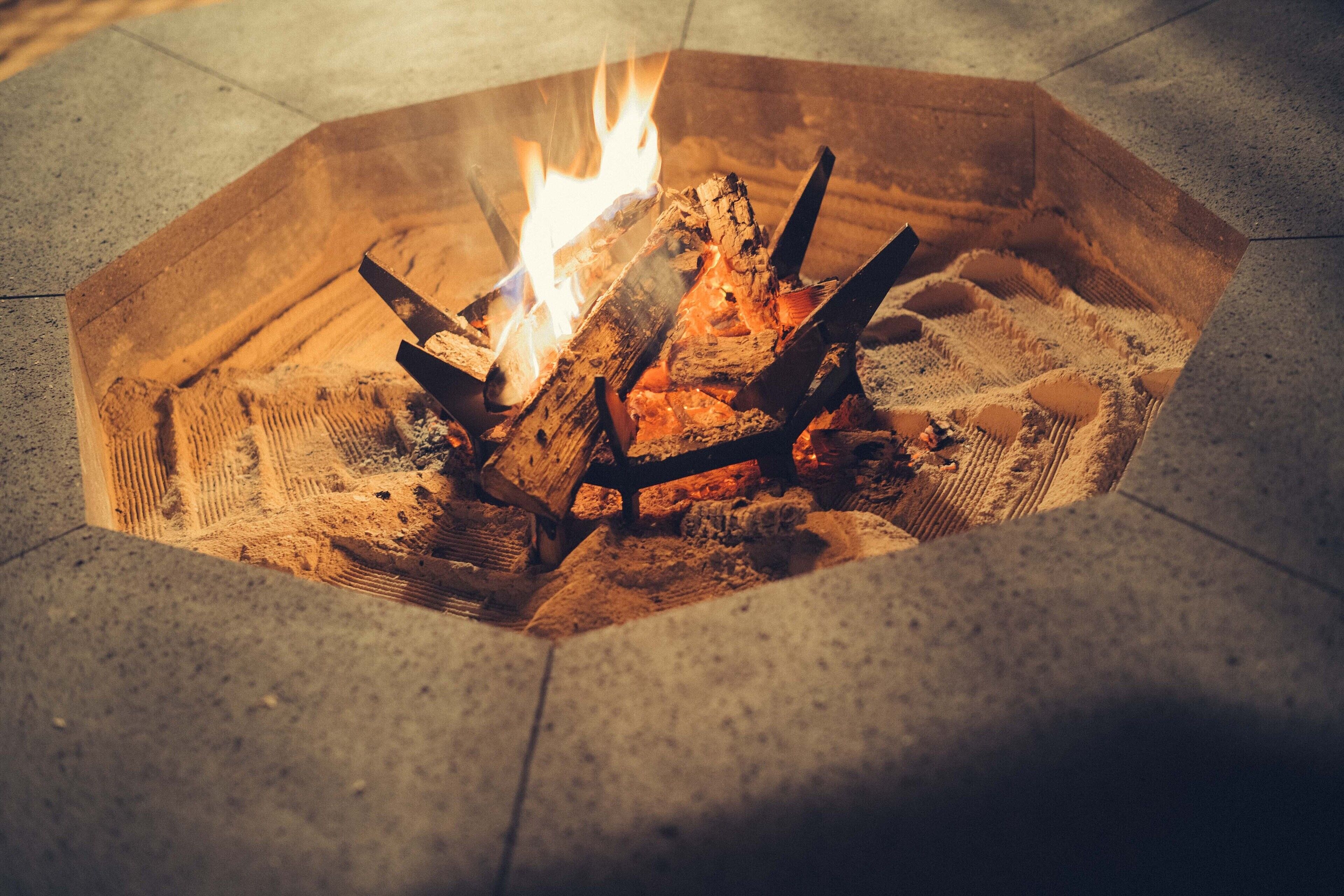 A fire pit with logs and flames, surrounded by a concrete floor.