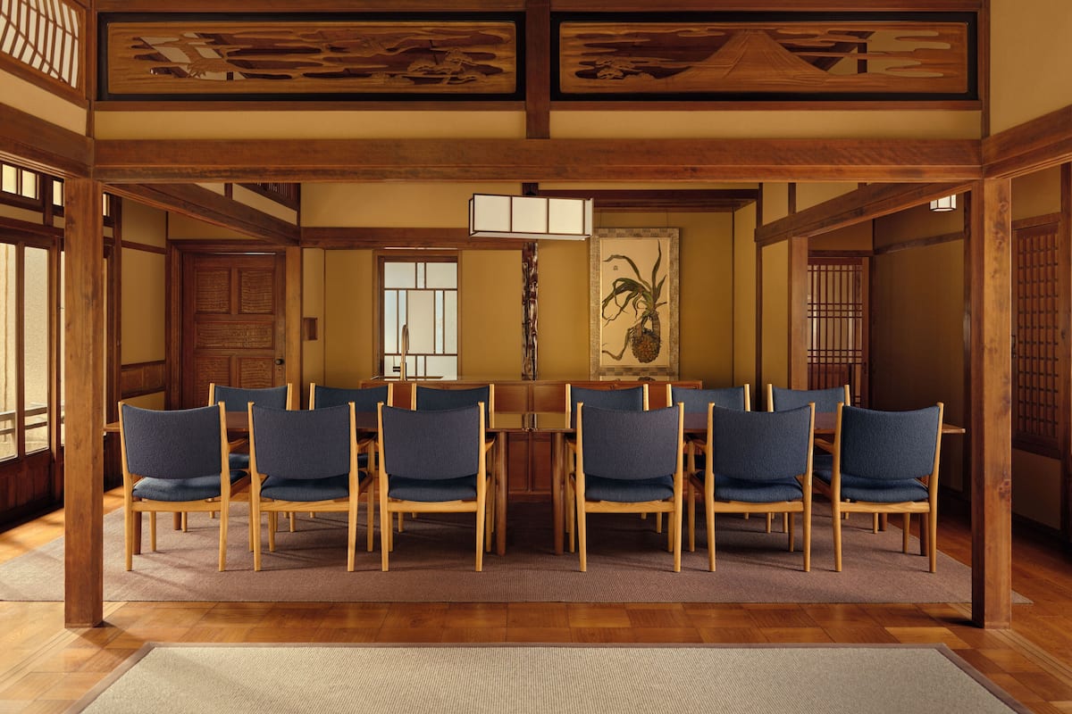 A traditional Japanese-style room with tatami flooring, a low wooden table surrounded by six chairs, and a shoji screen door.
