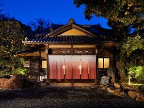 Perinteinen japanilainen rakennus, jossa on tiilikatto, puurakenne ja kivipolku, joka johtaa puiseen porttiin.