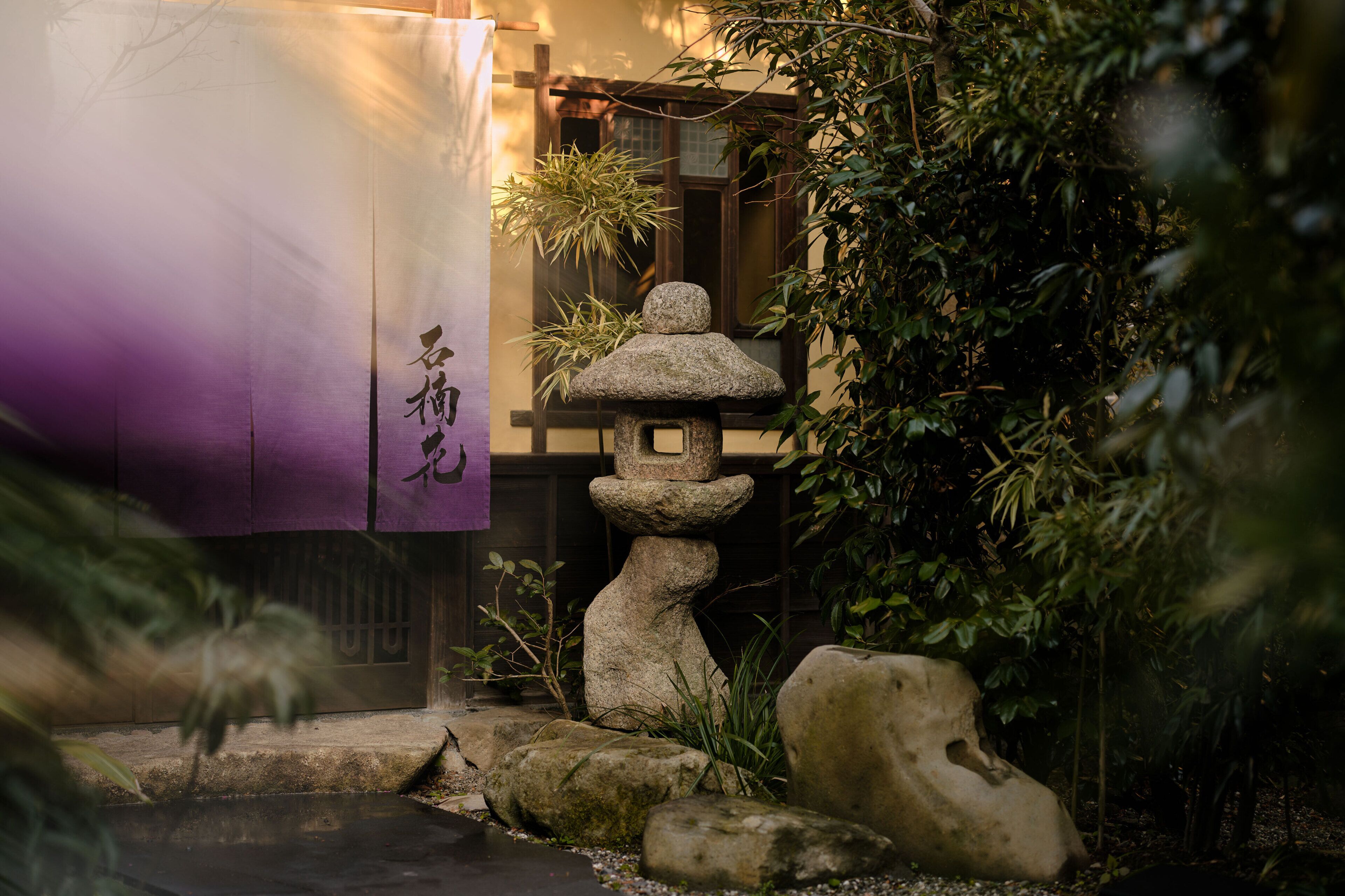 En traditionell japansk trädgård med en stenlykta, bambuväxter och en lila, hängande banderoll.