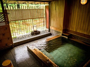 A traditional Japanese onsen with a wooden bench, a lantern, and a view of the outdoors through a bamboo screen. - Issinkan (Nikko)