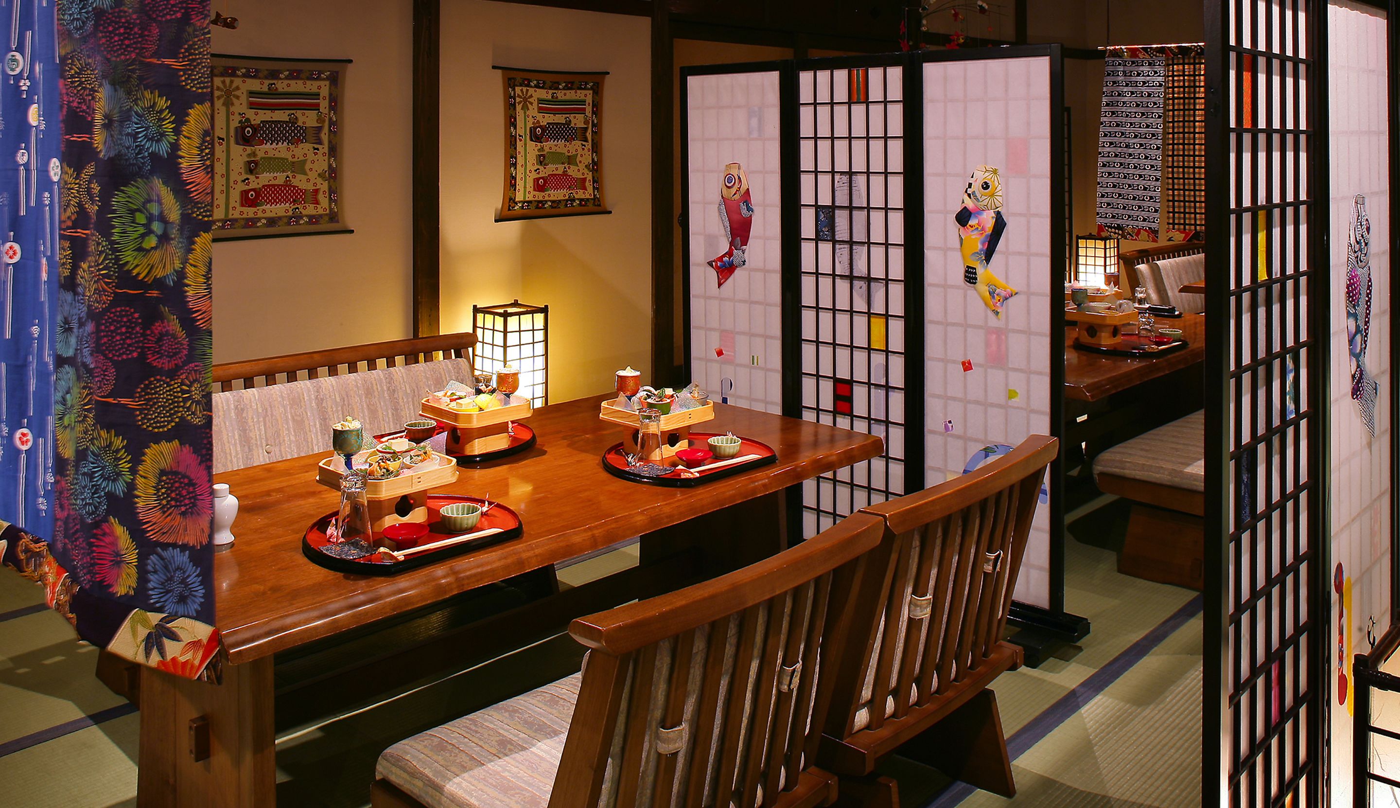 A traditional Japanese dining room with tatami mats, a low wooden table set with dishes, and sliding doors.