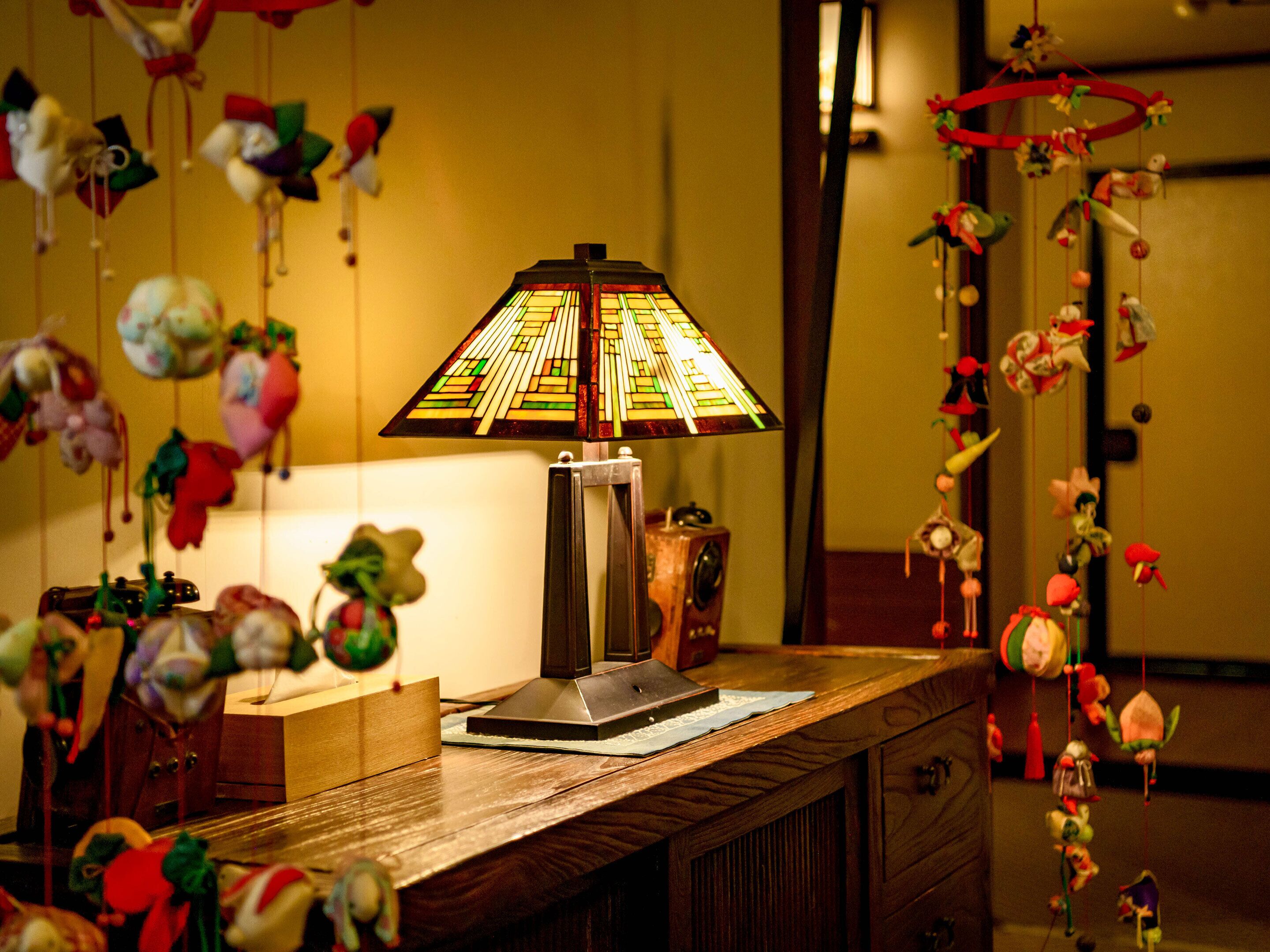 A wooden desk with a stained glass lamp, a vintage radio, and various hanging ornaments.