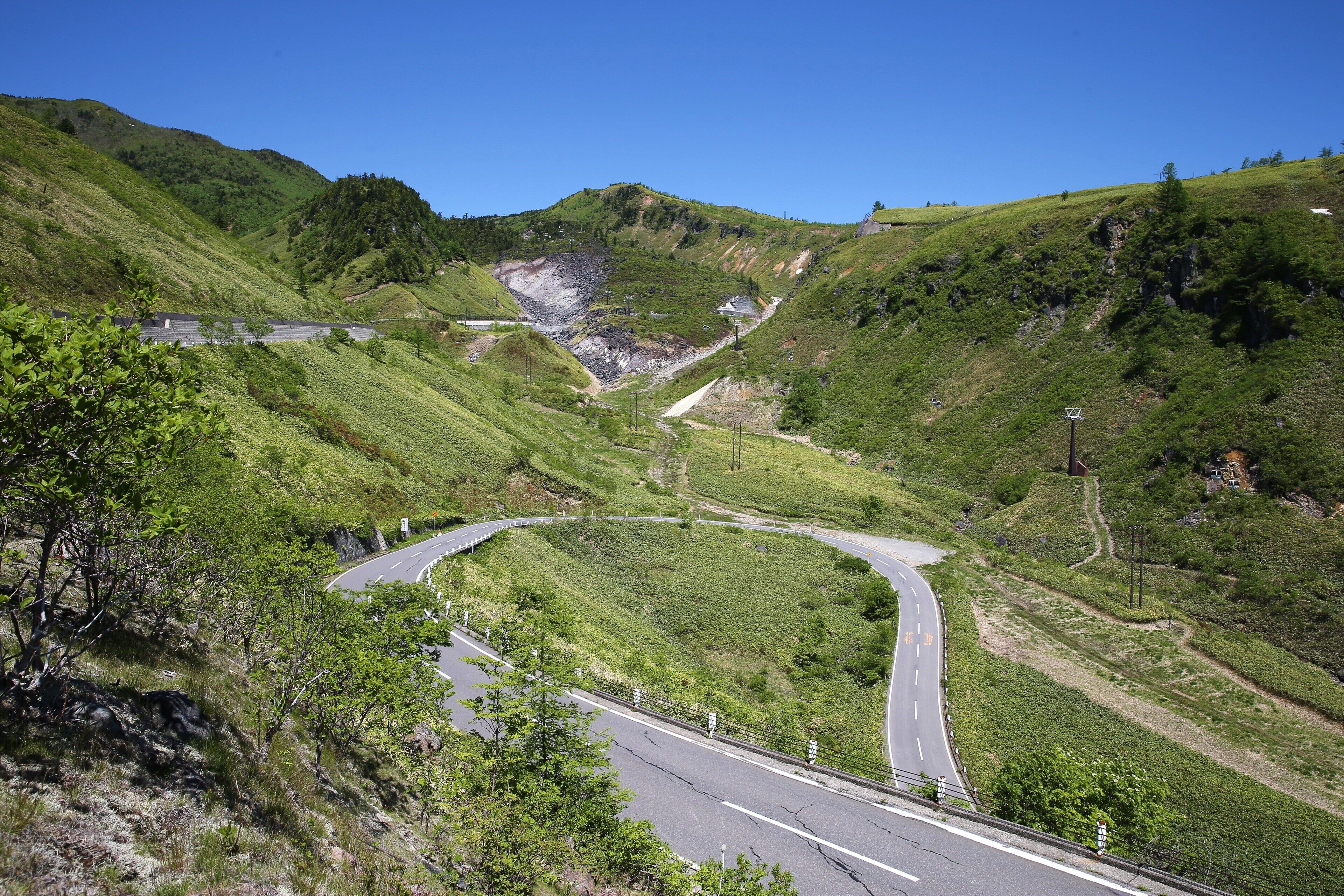 Uma estrada sinuosa por um vale verde com montanhas ao fundo.