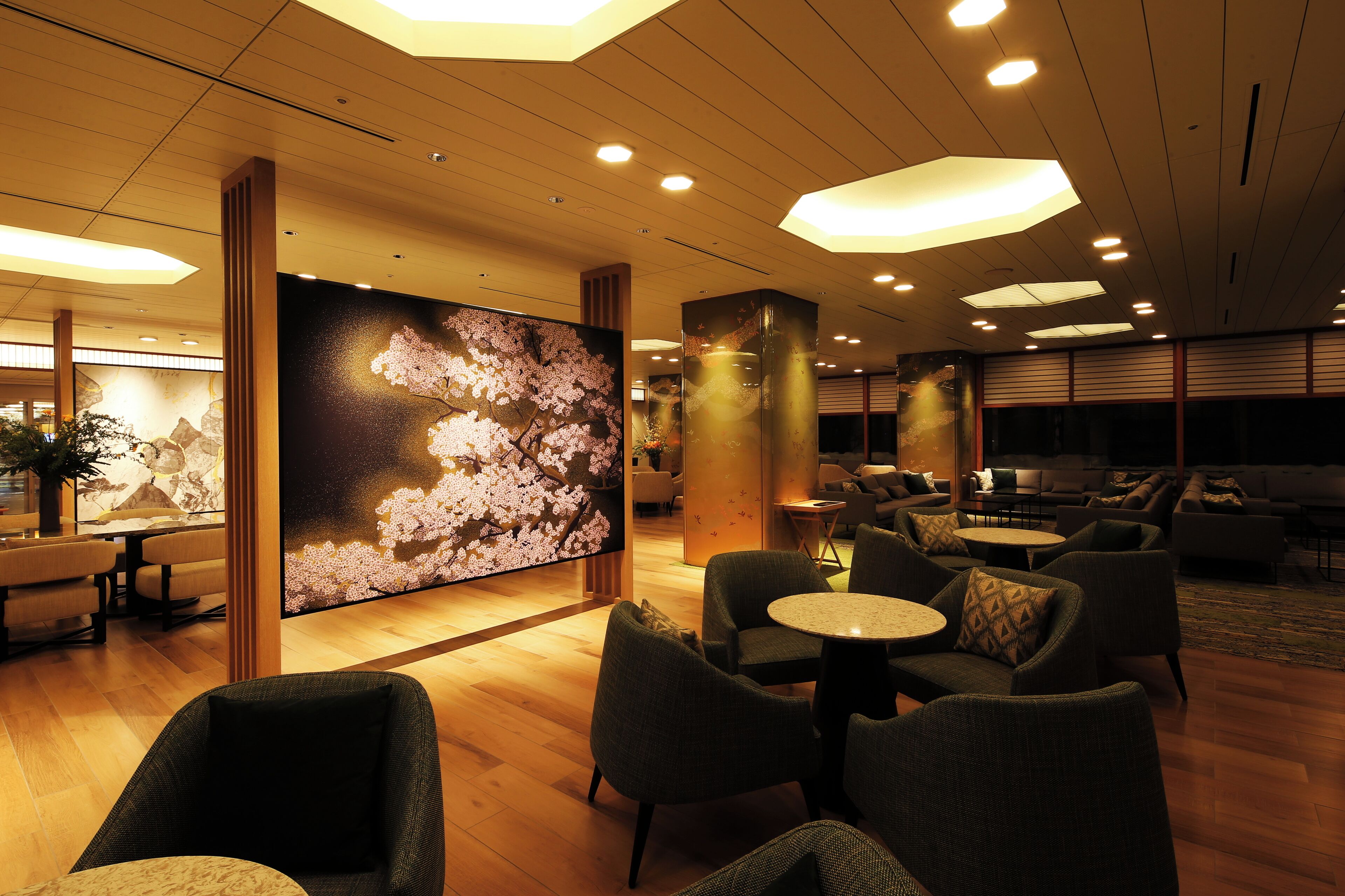 A spacious lobby with wooden flooring, multiple seating areas including sofas and chairs, and a large wall mural.