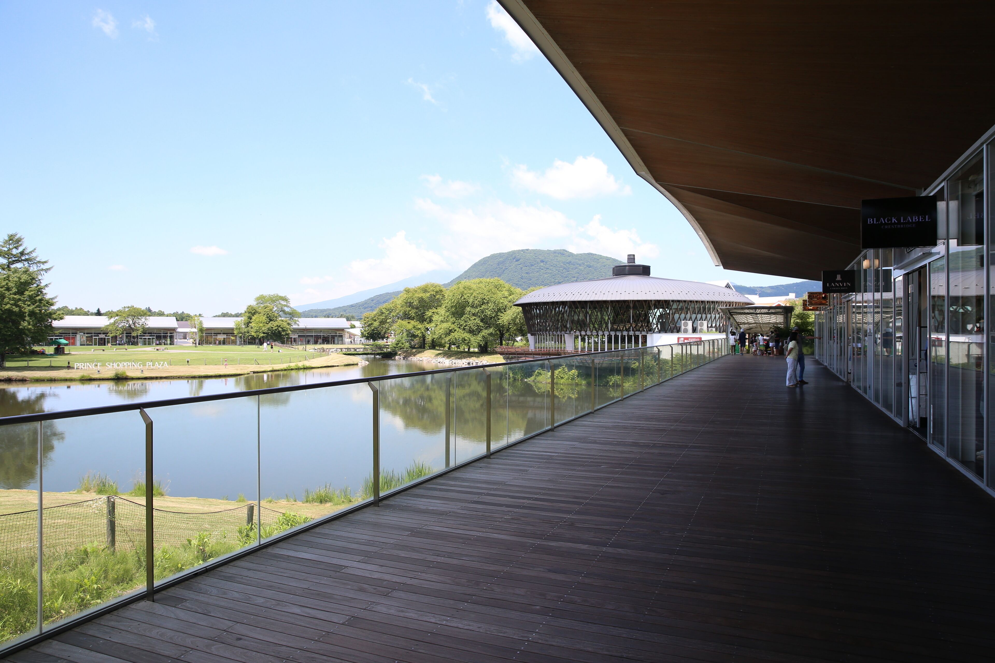 A wooden deck with glass railings overlooking a body of water and a park.