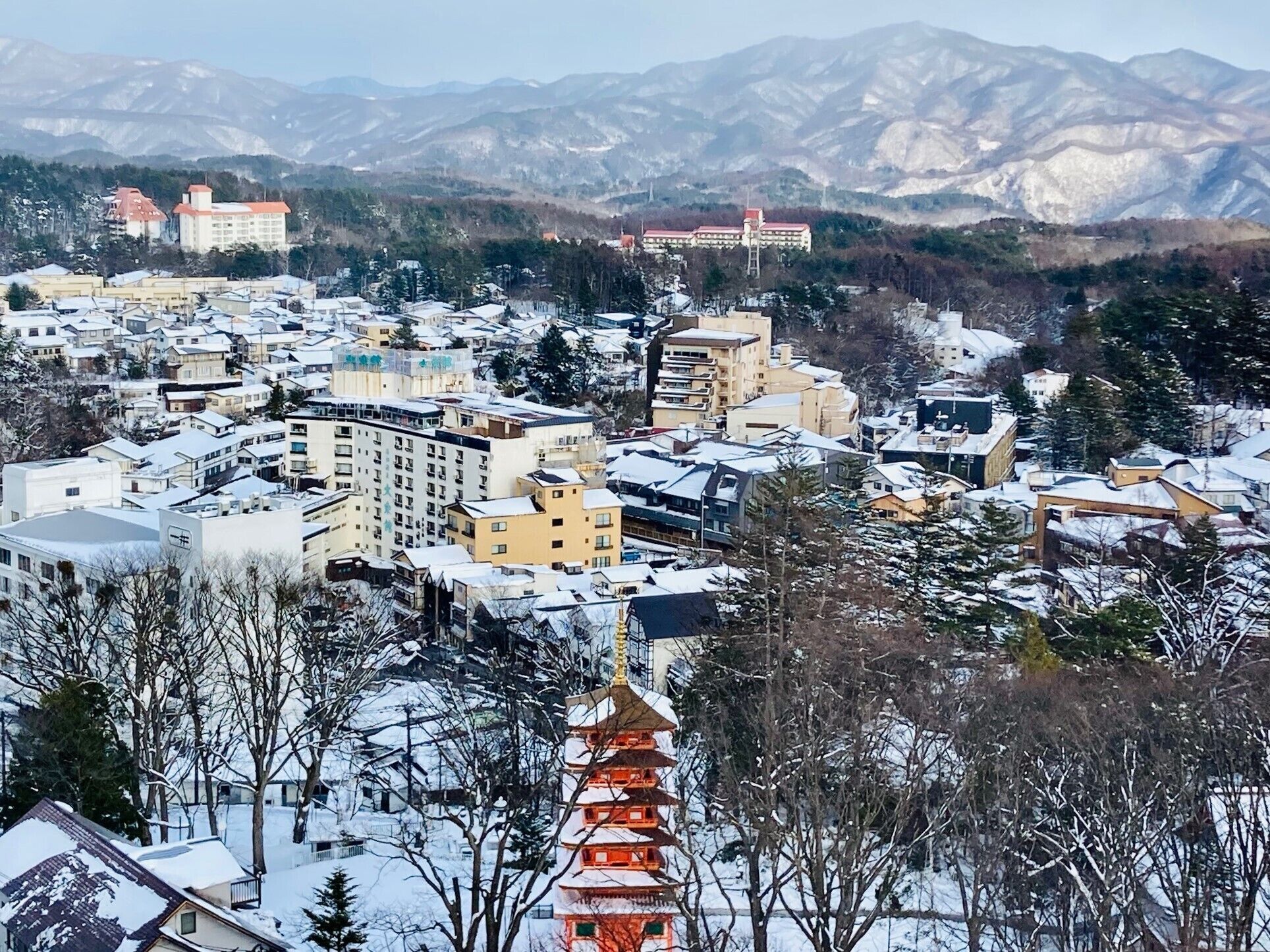 A snow-covered town with a prominent pagoda in the foreground, surrounded by residential buildings and mountains in the background.