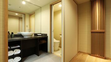 A modern bathroom with a large mirror, a sink, and a toilet. There are towels neatly folded on a shelf.