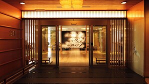Entrada de hotel con diseño tradicional, que presenta puertas correderas de vidrio, piso de madera y una gran obra de arte mural con motivos de cerezos en flor.