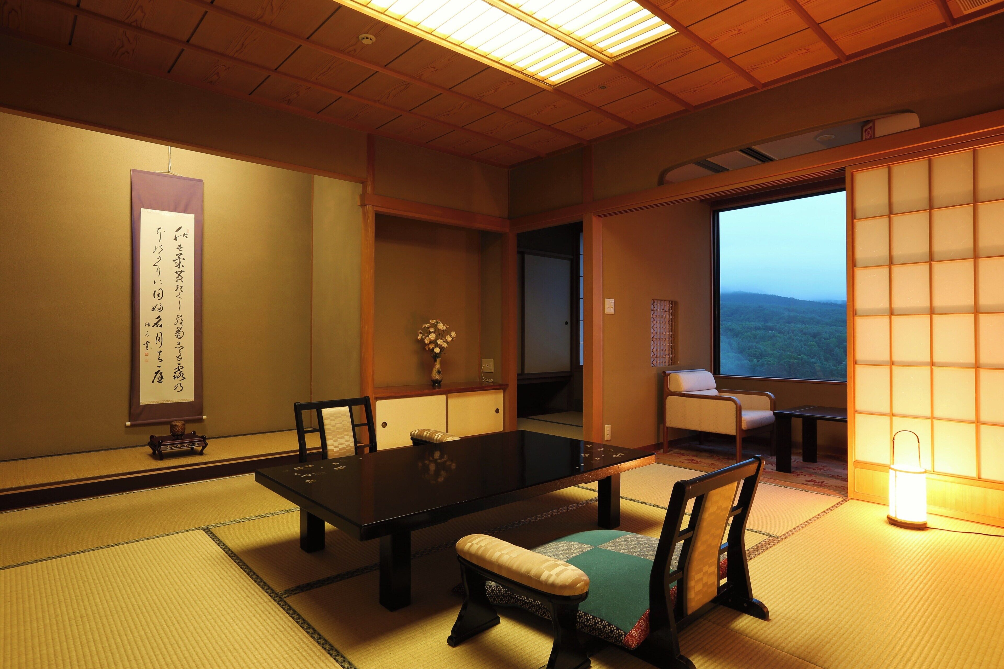 A traditional Japanese room with tatami flooring, a low table, and a sliding door leading to a balcony with a view of the mountains.