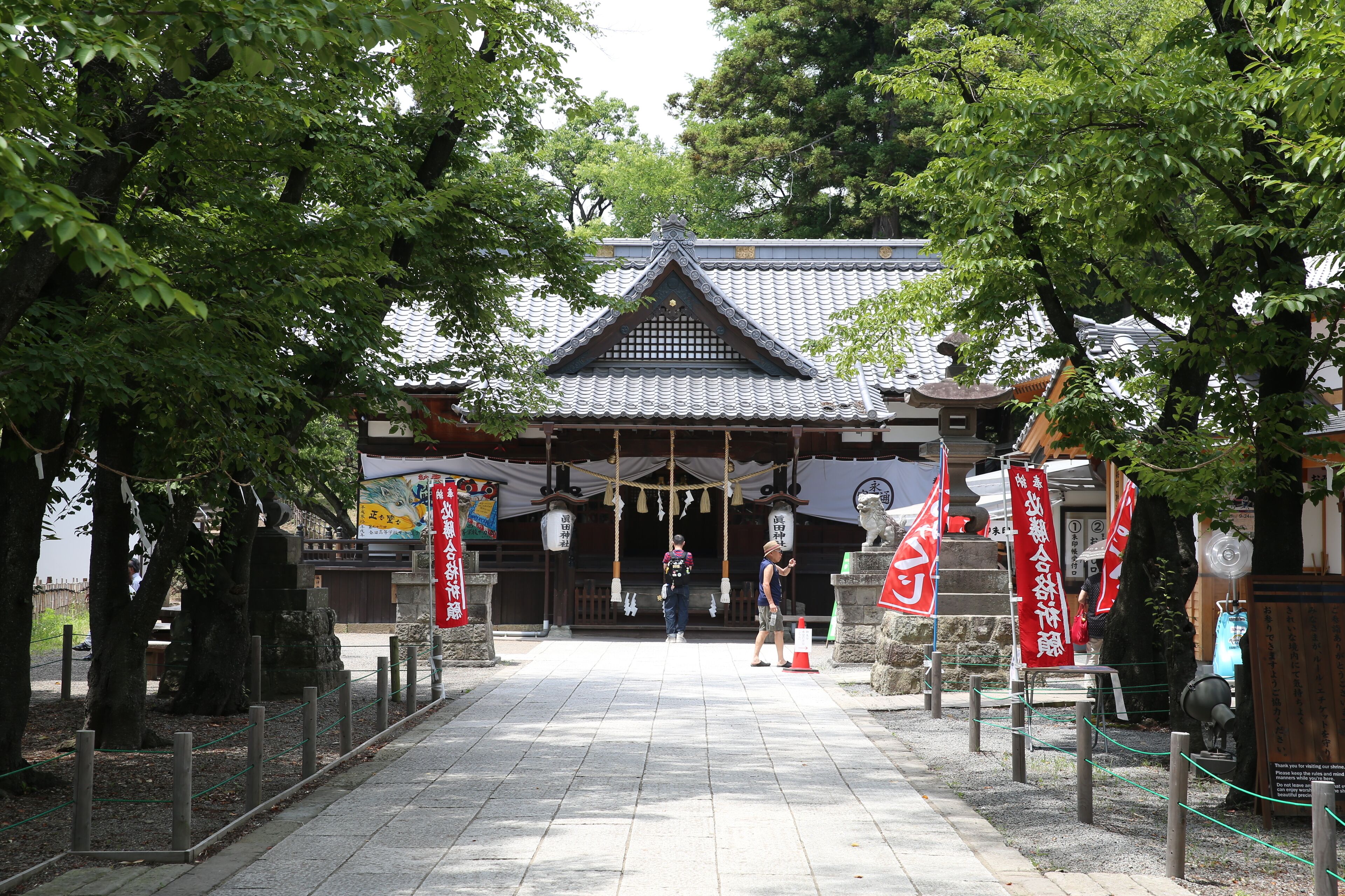 A traditional Japanese building with a tiled roof, surrounded by trees and stone lanterns.