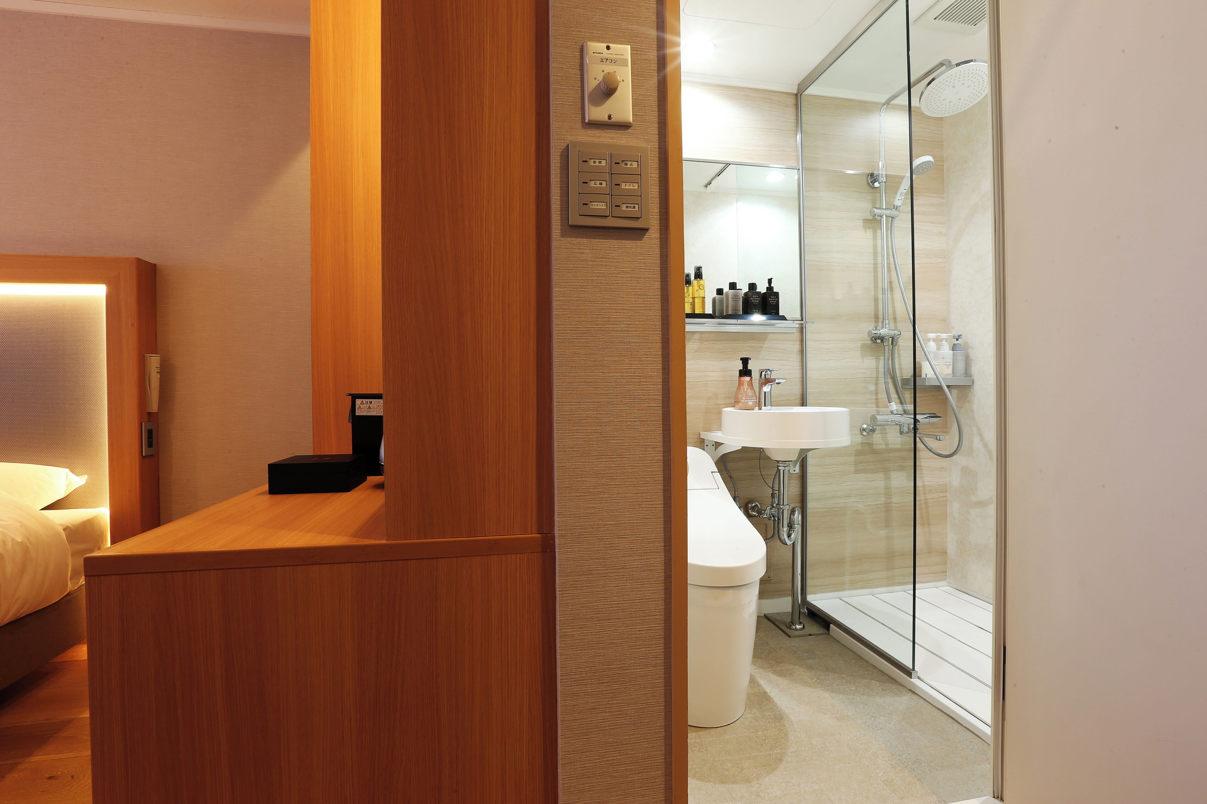 A hotel room with a wooden desk, a bed, a glass-enclosed shower, and a white sink.