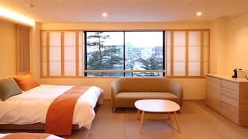 A hotel room with a bed, a sofa, a small table, a dresser, and a window with a view of trees and buildings.