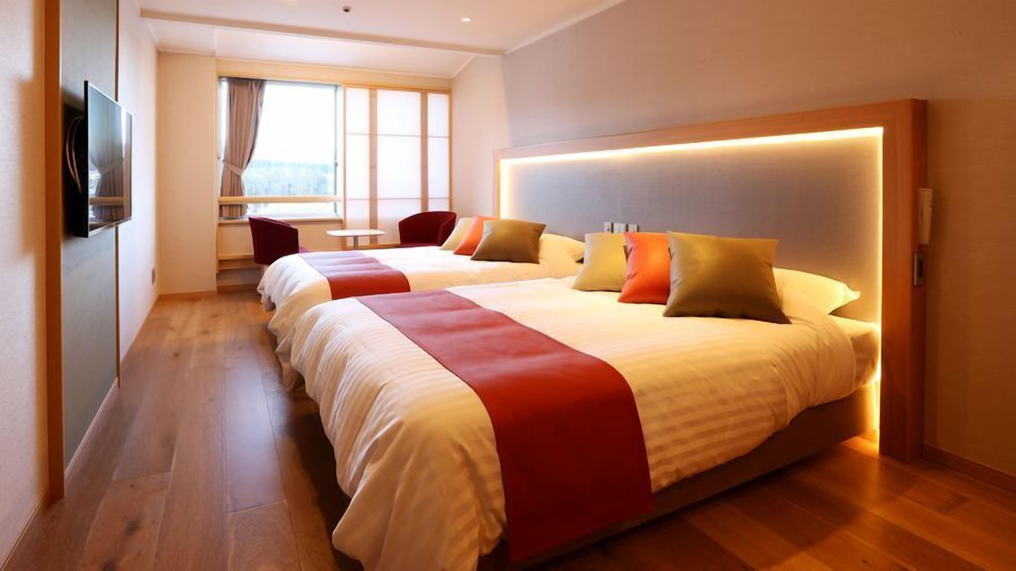 A hotel room with two beds, a TV, a window with curtains, and a wooden floor.