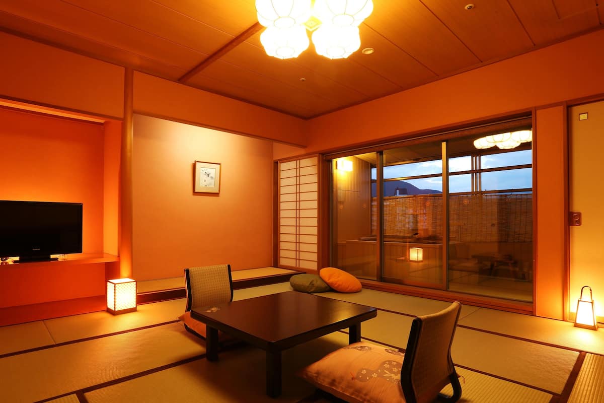 Une pièce de style japonais traditionnel, avec un sol recouvert de tatamis, une table basse, des chaises, un téléviseur et des portes coulissantes.