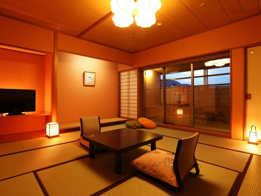 A traditional Japanese room with tatami flooring, a low table, chairs, a television, and sliding doors.