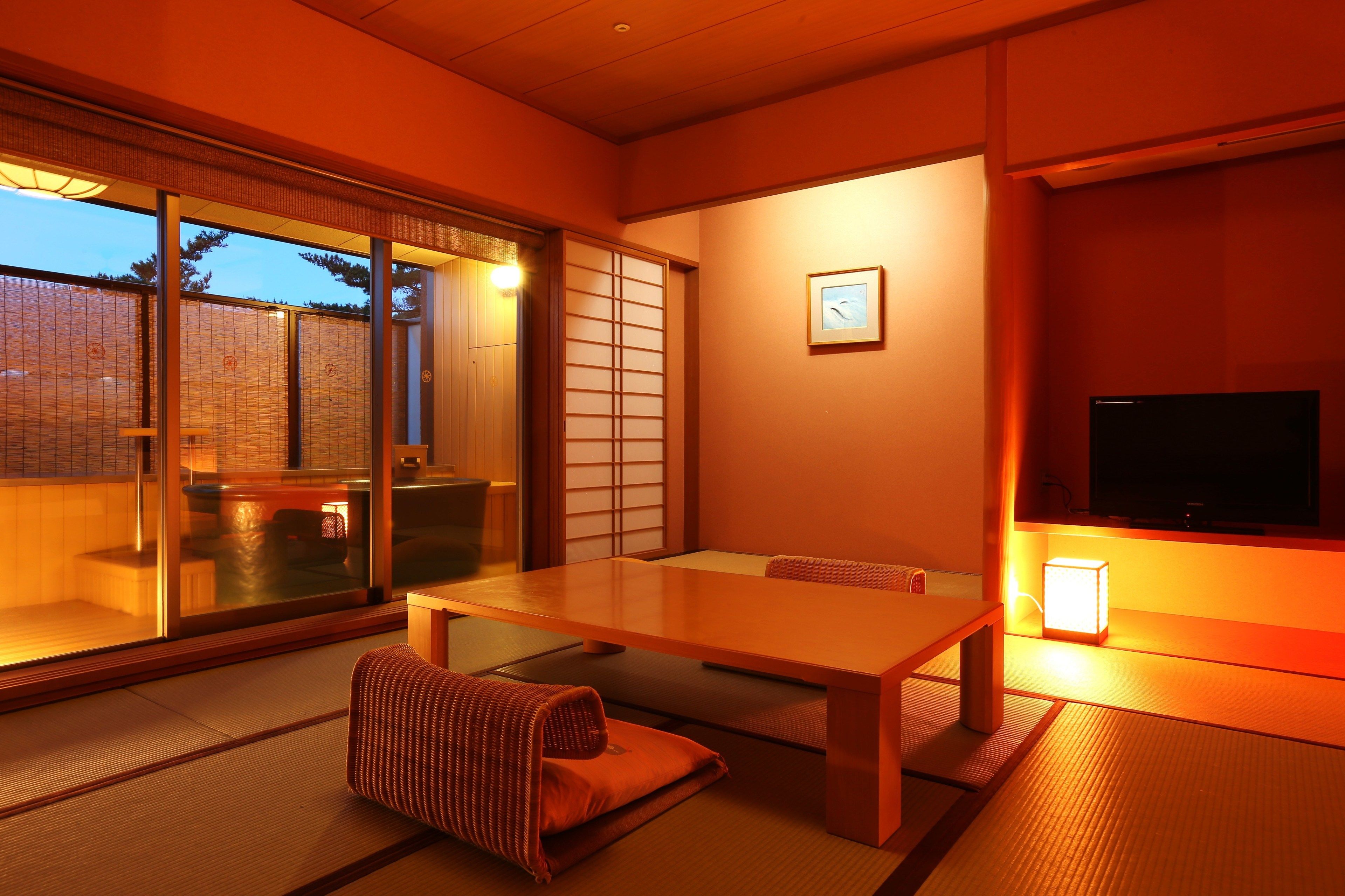 A traditional Japanese room with tatami flooring, a low table, a cushioned seating area, sliding doors, and a television.