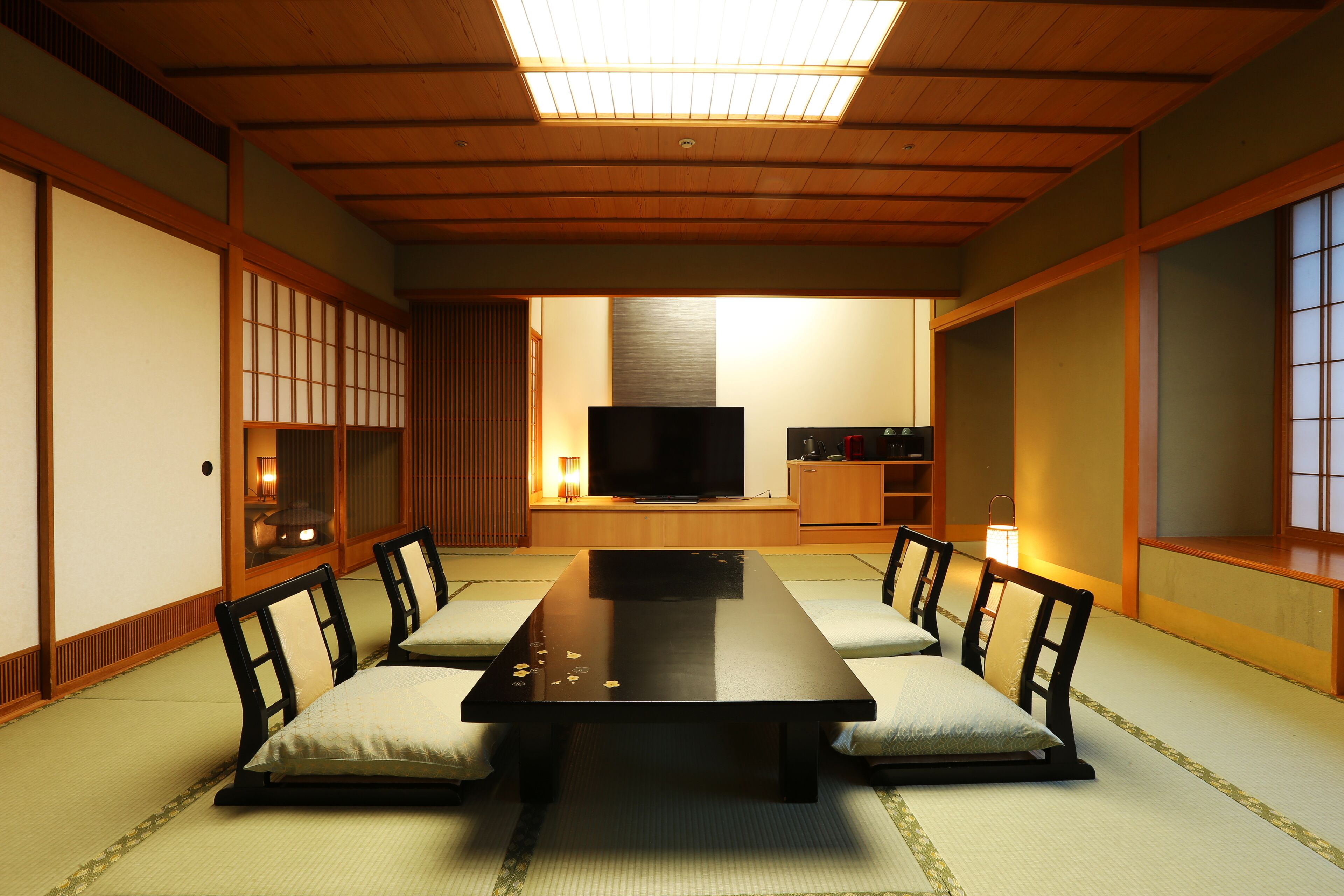 A traditional Japanese room with tatami flooring, a low table with cushions, a television, and sliding doors.