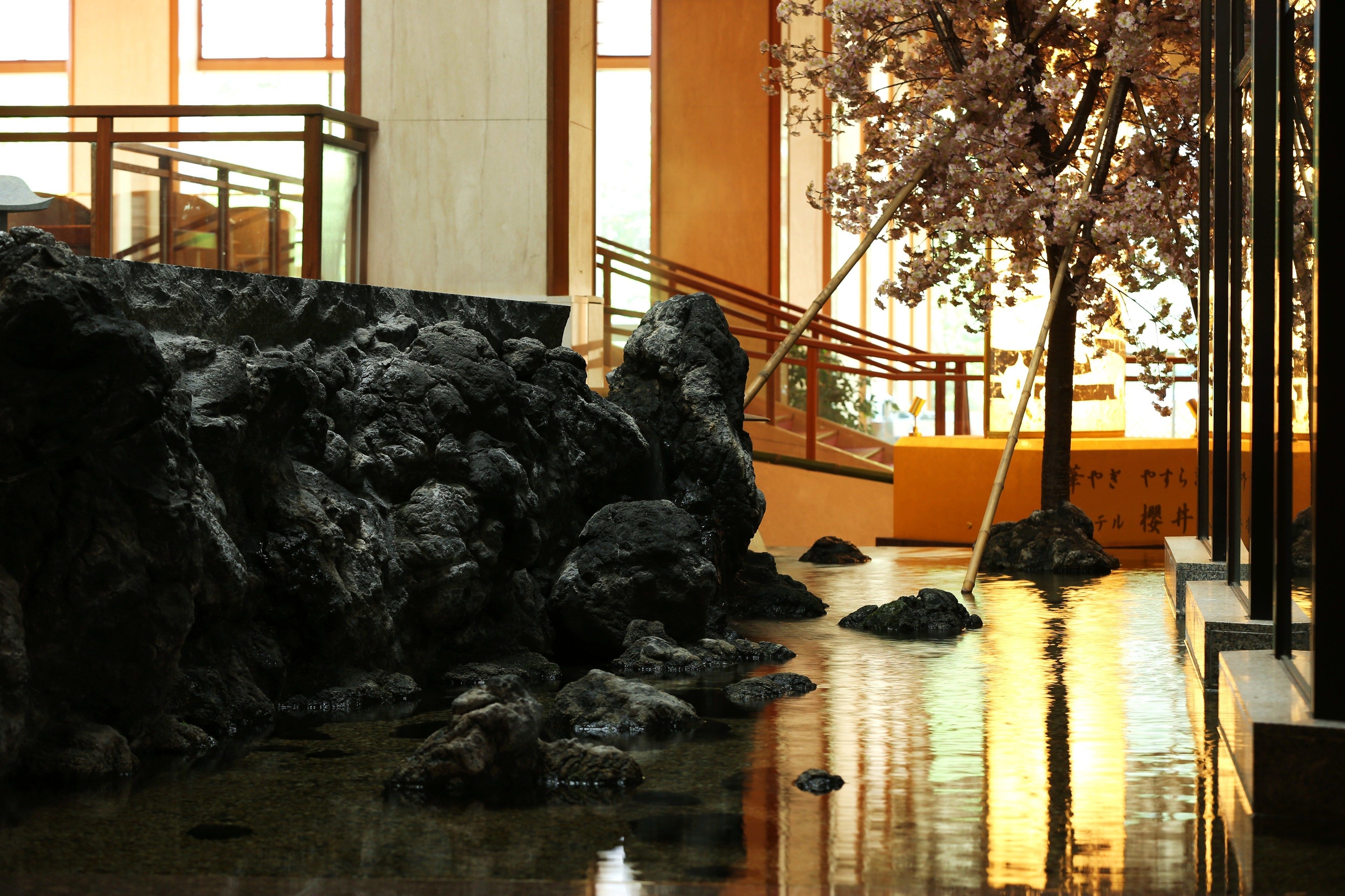 A serene indoor water feature with rocks and a cherry blossom tree.
