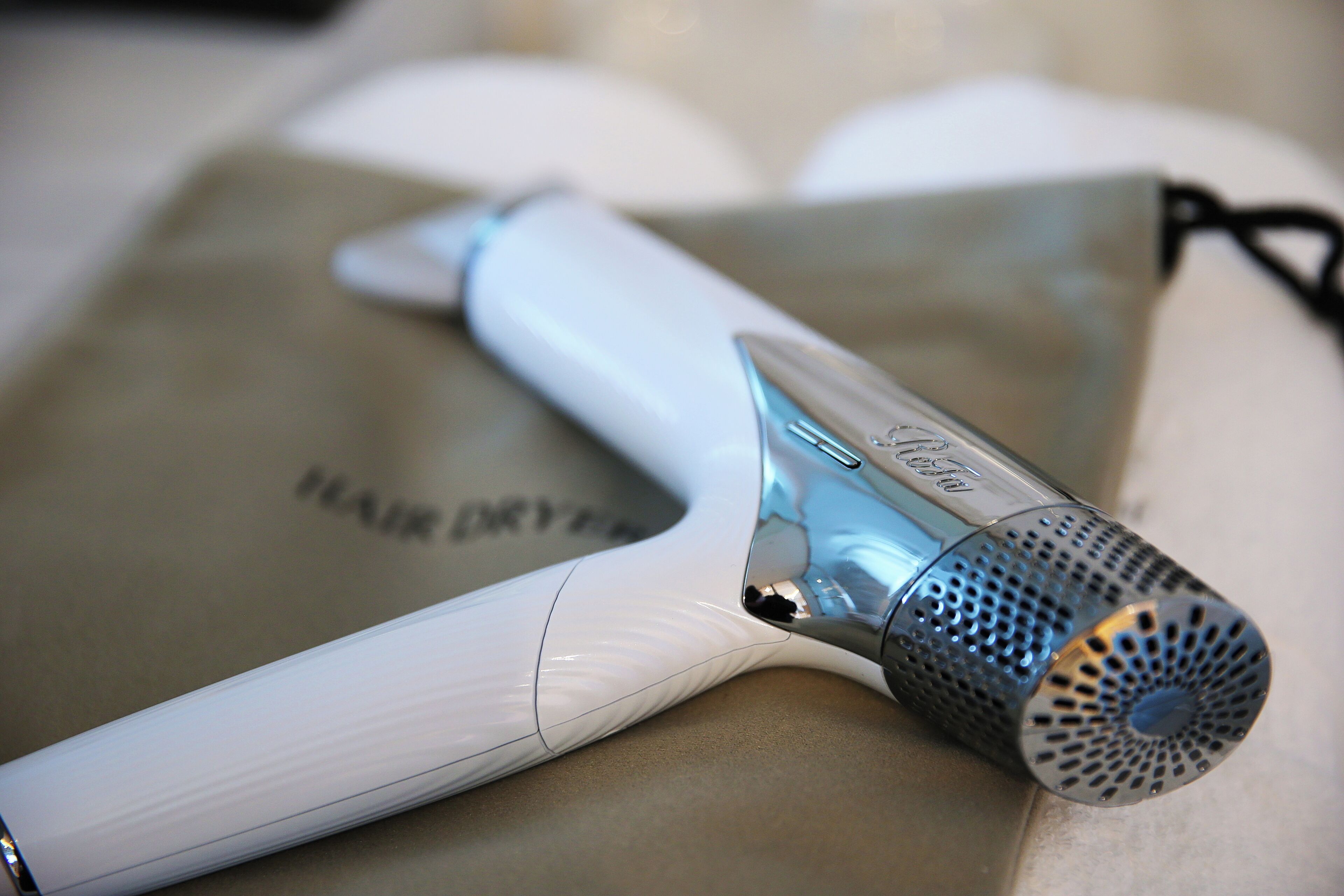 A hair dryer with a metallic nozzle and a white body, placed on a beige surface.