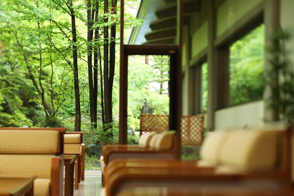 A row of wooden chairs with cushions, a wooden table, and a view of a forest through a glass door.