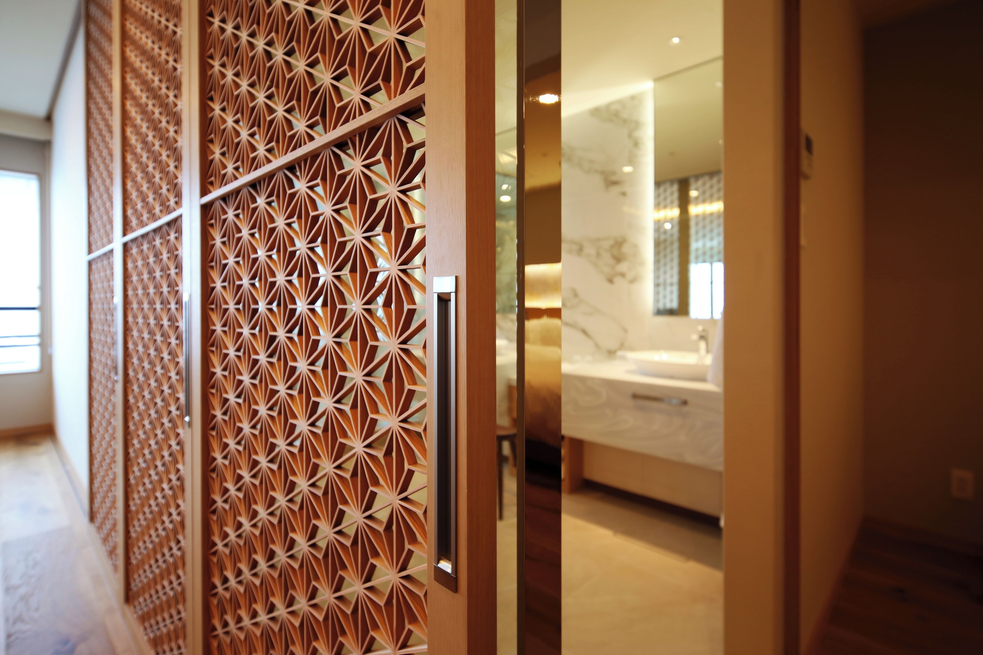 Ein modernes Hotelzimmer mit einer geometrisch gemusterten Trennwand, einem großen Bett und einem sichtbaren Badezimmer mit einer Badewanne.