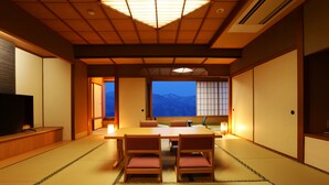 Una habitación japonesa tradicional con suelo de tatami, una mesa baja con sillas y un televisor a la izquierda.