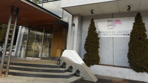 Entrada moderna de un edificio con fachada de vidrio, un alero de madera y un letrero para Breeze Bay Lake Resort Kawaguchiko.