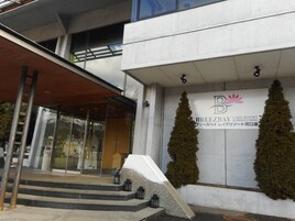 Entrada moderna de un edificio con fachada de vidrio, un alero de madera y un letrero para Breeze Bay Lake Resort Kawaguchiko.