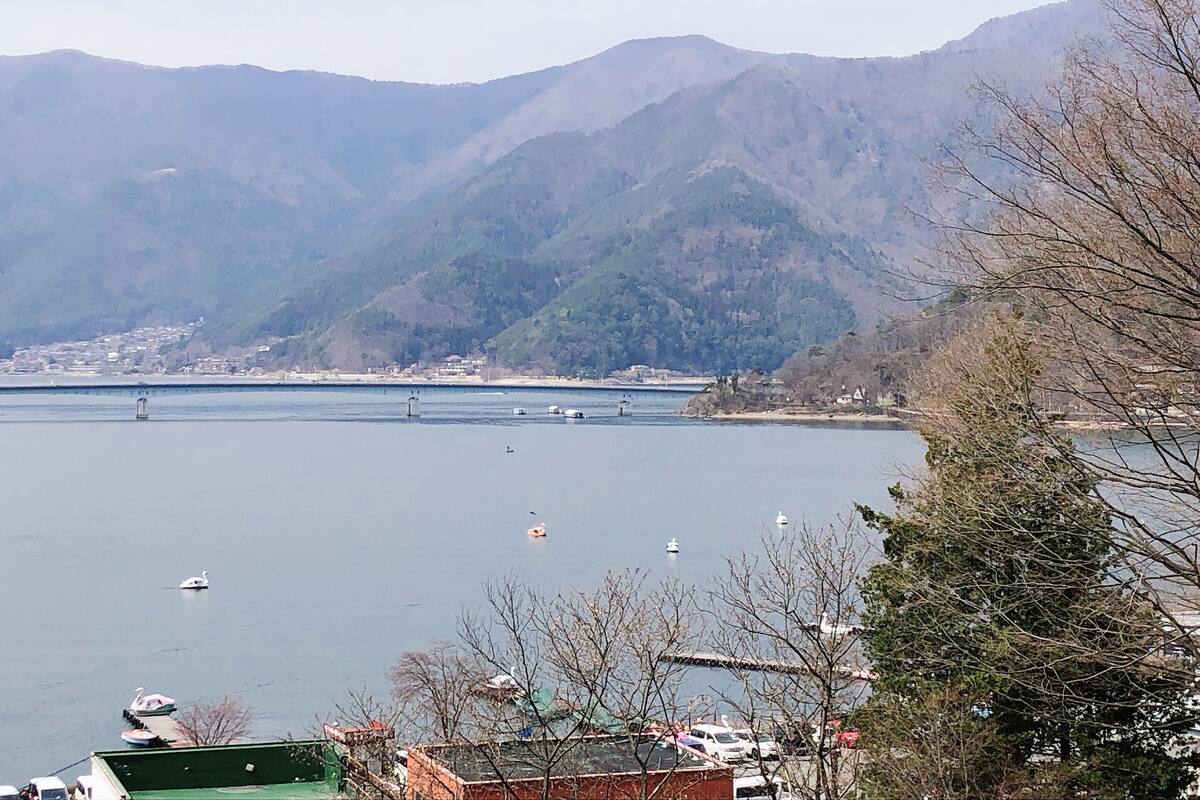 A view of a lake with boats, a bridge, and mountains in the background.