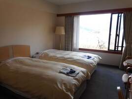 A hotel room with two beds, a desk, and a window with curtains.