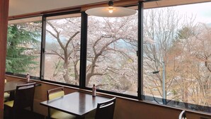 Un comedor con una mesa, sillas, una lámpara colgante y un amplio ventanal con vistas a flores de cerezo.