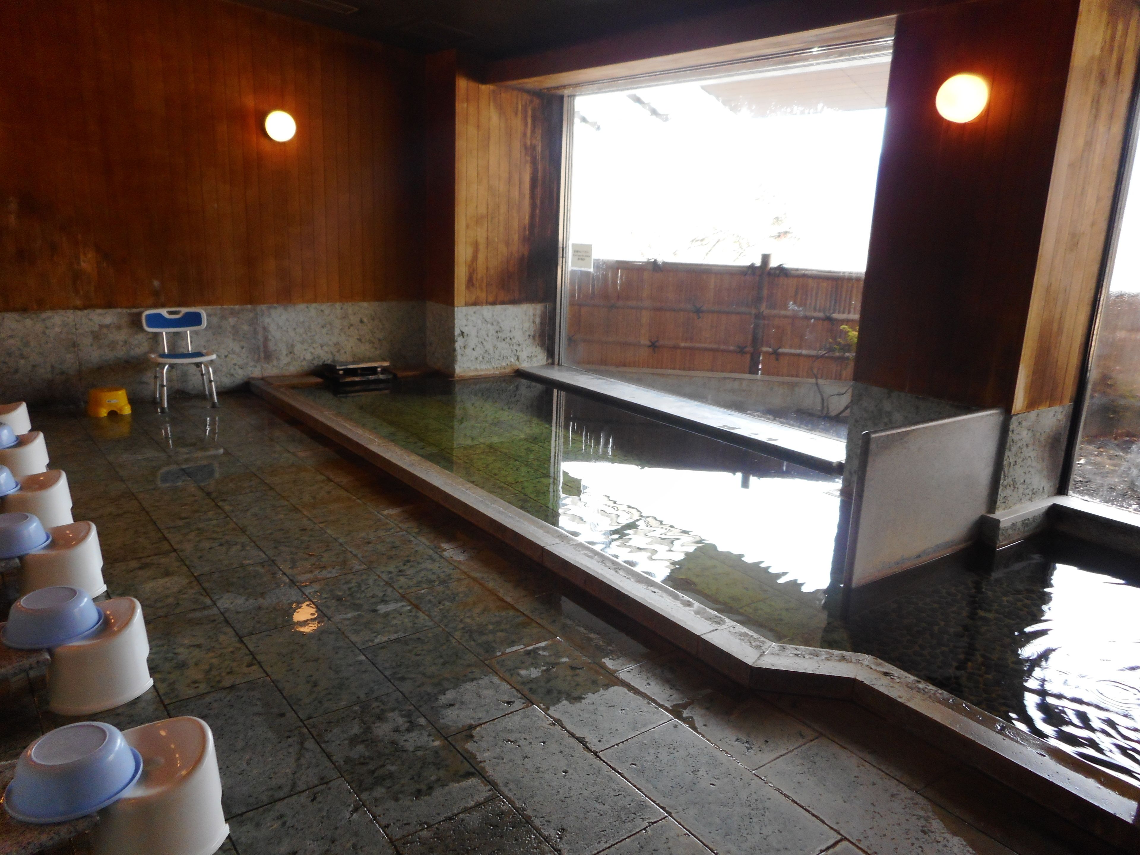 A room with a large rectangular pool, wooden walls, and a tiled floor.