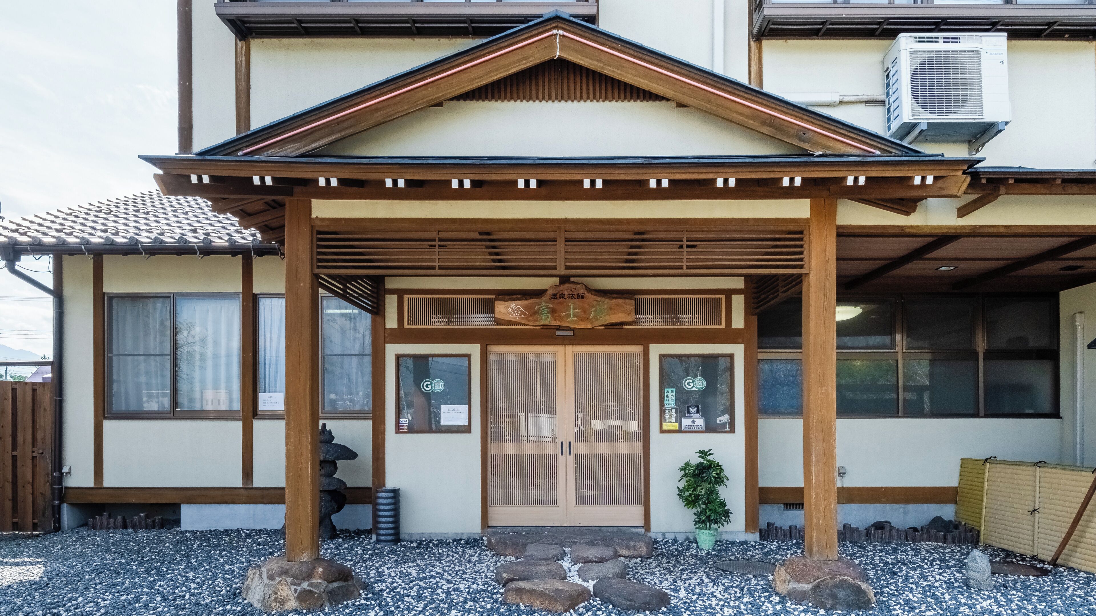 A traditional Japanese building with a wooden entrance, a covered porch, and a small garden area with rocks and a potted plant.
