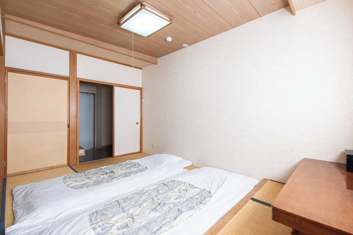 Una habitación con una cama, un escritorio de madera, un altavoz negro y una lámpara en el techo.