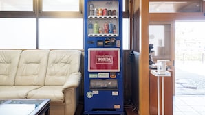 A vending machine with a Wonda coffee label, a beige sofa, and a small table with a white object on it. - Fujizakura Onsen Ryokan (Fuefuki)