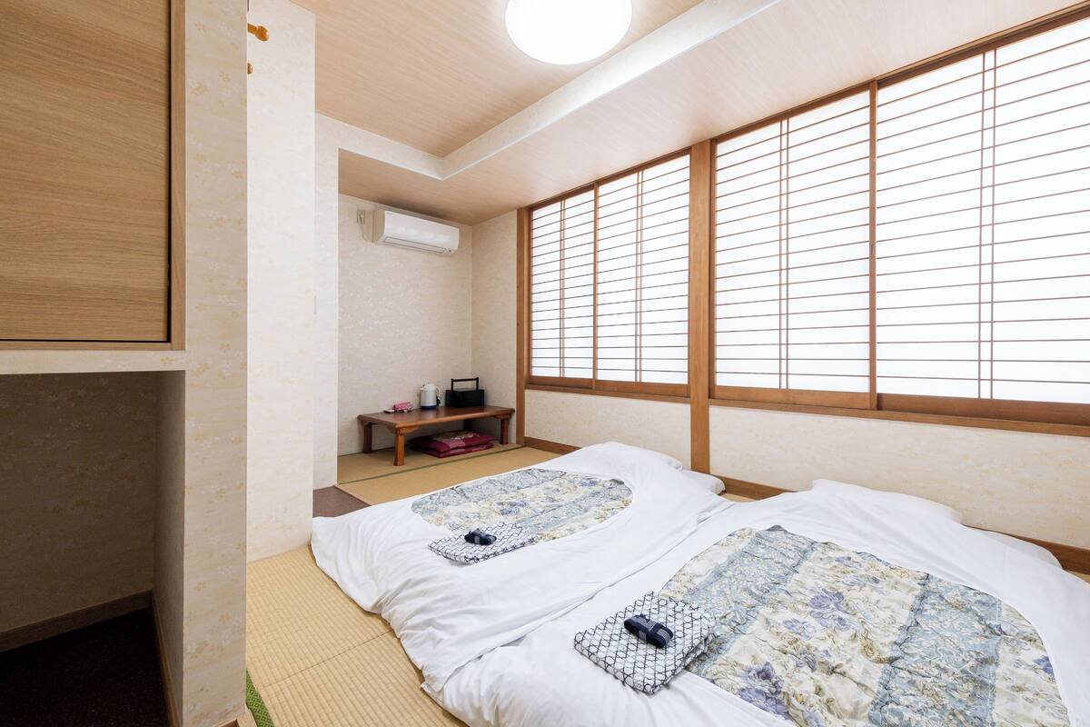 Una habitación tradicional japonesa con suelo de tatami, un futón, una mesita con hervidor y puertas correderas shoji.