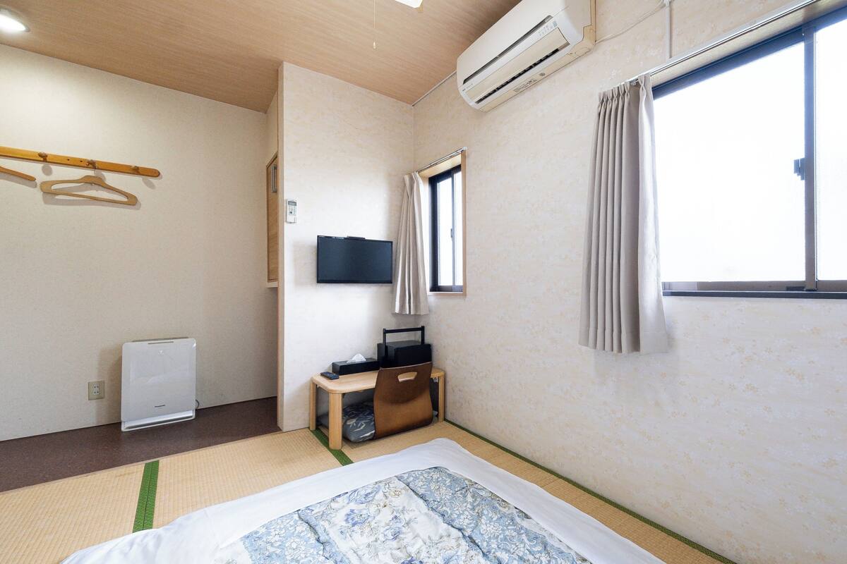Habitación de hotel con cama, televisión, escritorio, silla, ventana y aire acondicionado.