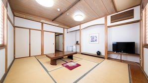 A traditional Japanese room with tatami flooring, a low wooden table, a television on a shelf, and a framed picture on the wall. - Fujizakura Onsen Ryokan (Fuefuki)
